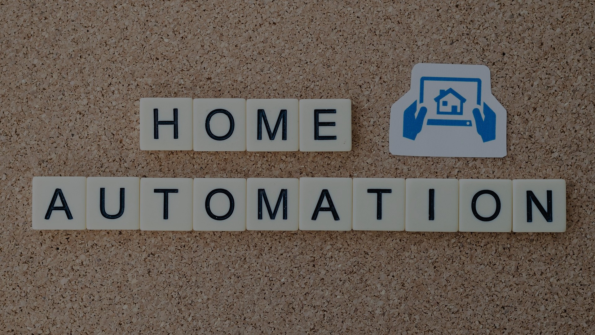 Image of scrabble tiles saying Home Automation and a sticker with blue hands holding a tablet with an image of a home on it